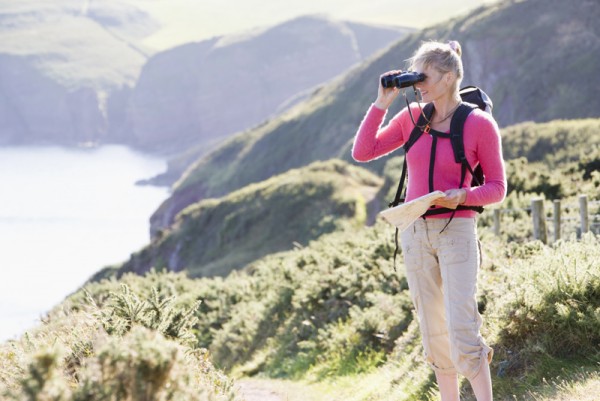 Woman on cliffside path using binoculars