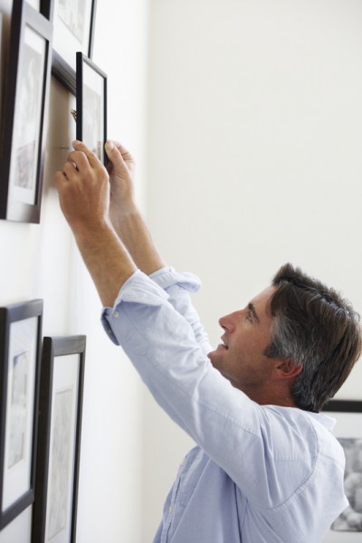 Man Hanging Picture Frames On Wall At Home