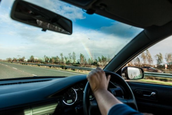 Male driver hands holding steering wheel of a car and road