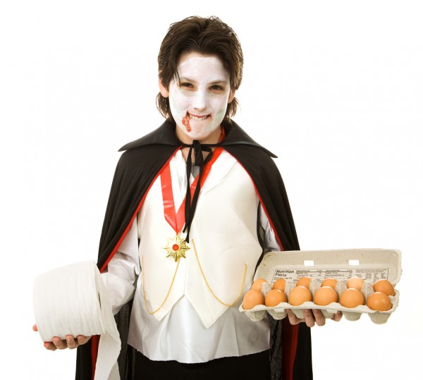 Mischievous adolescent boy ready to play halloween tricks with eggs and toilet paper. Isolated on white.