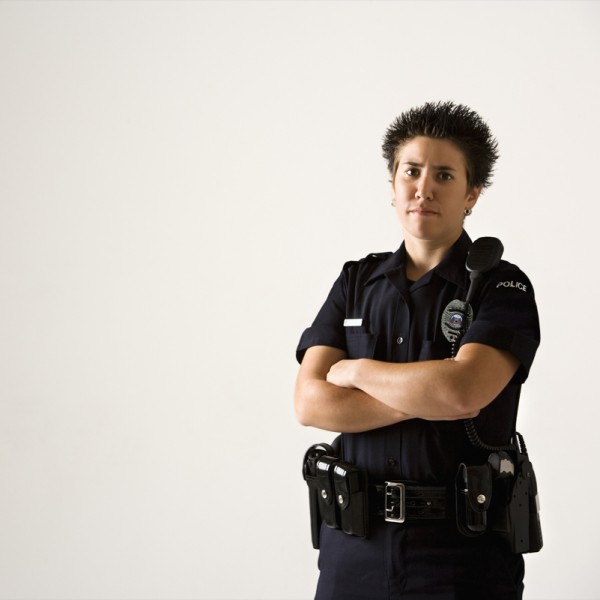 Portrait of mid adult Caucasian policewoman standing with hand on gun holster looking at viewer.