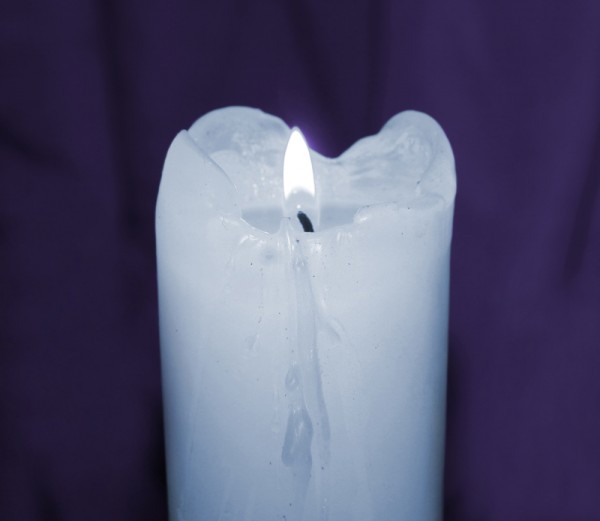 Glowing mourning candle taken closeup on purple.